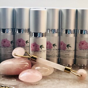May include: A collection of silver-topped bottles with labels featuring a pink peony design. A rose quartz face roller and several rose quartz stones are displayed in front of the bottles. The bottles are for carrier oils.