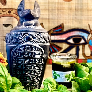May include: A black, Egyptian-style jar with hieroglyphs and a cat-like head, next to a small glass jar of green liquid labeled "Basil Concrete" and surrounded by fresh basil leaves. The background features Egyptian art.