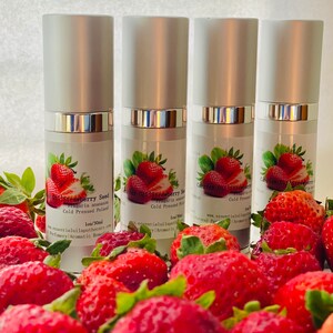 May include: Four silver and white essential oil bottles with labels featuring strawberries and text. The bottles are surrounded by fresh, ripe strawberries. The labels read "Strawberry Seed Fragaria ananassa Cold Pressed Poland 1oz/30ml".
