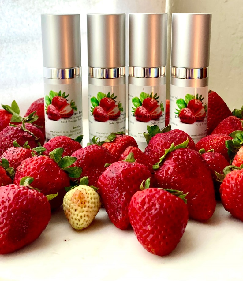 May include: Four silver-topped spray bottles with labels featuring a strawberry design, surrounded by fresh, ripe red strawberries. The bottles are labeled "Strawberry Serum" and "Cold Pressed".