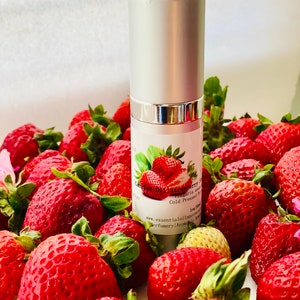 May include: A silver bottle of strawberry oil with a label featuring a strawberry illustration, surrounded by fresh, ripe strawberries. The bottle is labeled "Carrier Oil Strawberry Seed".