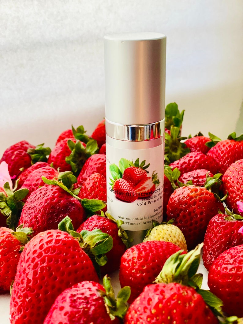 May include: A silver bottle of strawberry oil with a label featuring a strawberry illustration, surrounded by fresh, ripe strawberries. The bottle is labeled "Carrier Oil Strawberry Seed".