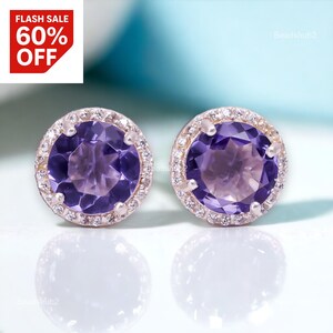 Peut inclure: Boucles d'oreilles à clous avec de grosses pierres violettes rondes, chacune entourée d'un halo de petites pierres claires. Les boucles d'oreilles sont serties dans un métal argenté. Une bannière rouge et blanche "FLASH SALE 60% OFF" est en haut à gauche.