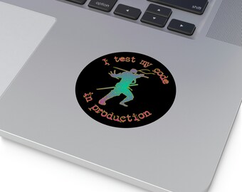 May include: A black and white sticker with a silhouette of a ninja holding a sword. The text "I test my code in production" is written in a rainbow gradient.