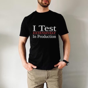 May include: A black short-sleeved t-shirt featuring the white text I Test, the red text EXTENSIVELY, and the white text In Production. The shirt has a crew neckline and a standard fit, displaying a humorous message about software development.