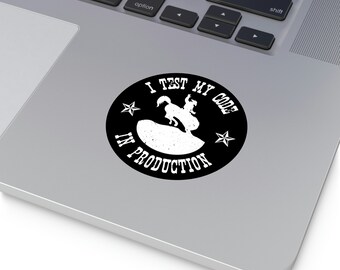 May include: A black and white sticker with a cowboy riding a bucking bronco. The sticker says "I test my code in production" with stars on either side of the text.