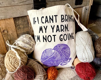 May include: A white canvas tote bag with the text "If I can't bring my yarn, I'm not going." The bag is filled with balls of yarn in various colors, including beige, white, and purple.
