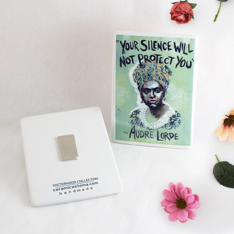 May include: White ceramic tile with a black and white image of a woman wearing a head wrap. The tile has the text "Your Silence Will Not Protect You" and "Audre Lorde" printed on it. The tile is part of the Sisterhood Collection and is handmade.