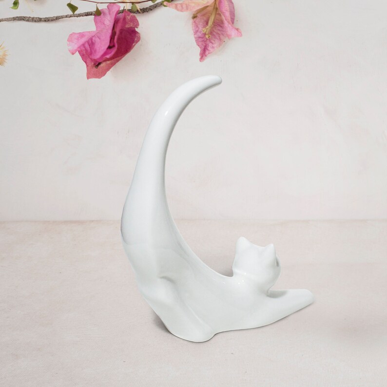 May include: White ceramic cat figurine with a curved tail, standing on a white surface.