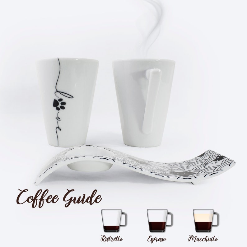 Puede incluir: Dos tazas de caf&eacute; de cer&aacute;mica blanca con dise&ntilde;os de huellas de patas negras y la palabra "Love" en una taza. Las tazas est&aacute;n sobre un platillo de cer&aacute;mica blanca con un patr&oacute;n blanco y negro. La imagen tambi&eacute;n incluye una gu&iacute;a de caf&eacute; con ilustraciones de diferentes bebidas de caf&eacute;: Ristretto, Espresso y Macchiato.