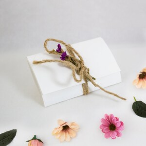May include: A white envelope tied with twine and decorated with small purple flowers. The envelope is surrounded by small pink and peach flowers and green leaves.