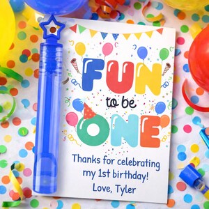 May include: A blue bubble wand with a star-shaped top and a birthday card that says "FUN to be ONE". The card has colorful balloons and confetti, with the text "Thanks for celebrating my 1st birthday! Love, Tyler."