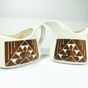 May include: A white ceramic creamer and sugar bowl set with a brown geometric pattern. The pattern features triangles and lines.