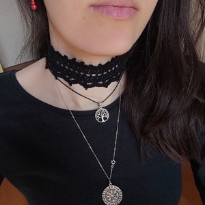 May include: A black lace choker necklace with a silver chain and two pendants. The top pendant is a tree of life design and the bottom pendant is a circular compass with runes.