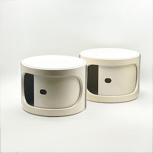 May include: Two matching, cream-colored side tables with a rounded design. Each table has a circular top and a curved front with a small, oval-shaped opening. The tables are approximately 18 inches in diameter and 16 inches tall.