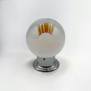 May include: A frosted glass globe light fixture with a chrome base. The light bulb inside is visible and has a warm orange glow.