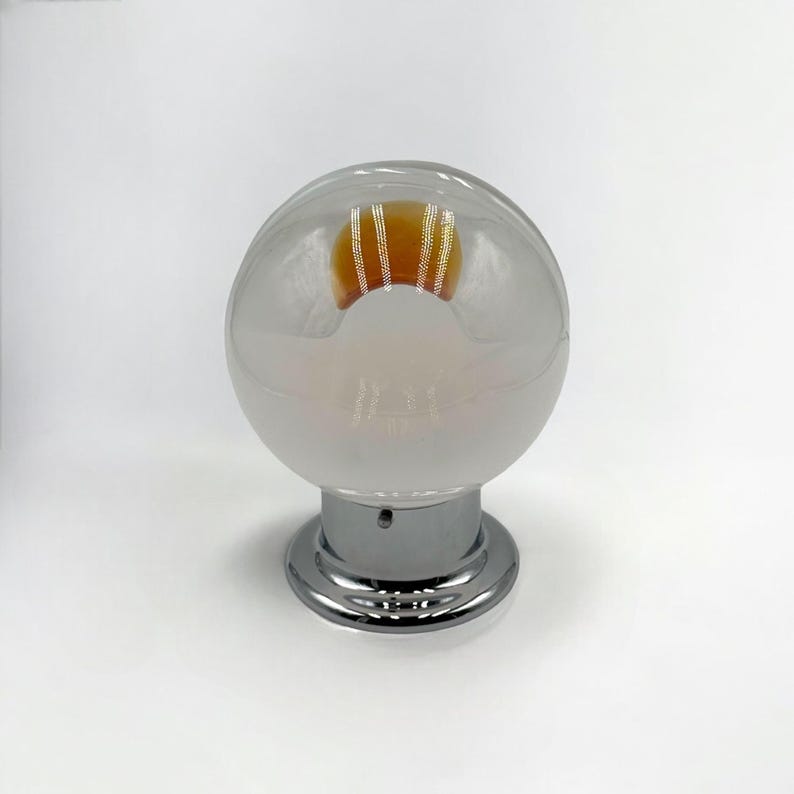 May include: A frosted glass globe light fixture with a chrome base. The light bulb inside is visible and has a warm orange glow.