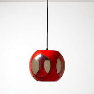 May include: A red pendant light fixture with a spherical shape and three circular, clear panels. The light hangs from a black cord against a white background. The fixture has a retro, mid-century modern design.