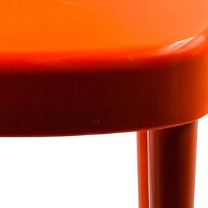May include: Close-up of a bright orange chair with a rounded seat and legs. The chair's color transitions from a vibrant orange on top to a deep red at the base, creating a gradient effect. The legs are cylindrical and the background is white.