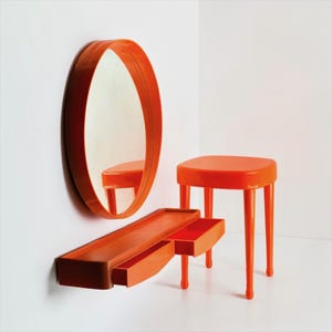 May include: An orange, modern vanity set with an oval mirror, a shelf with a drawer, and a small stool. The mirror is mounted on the wall, and the shelf is attached below it. The stool has four legs.