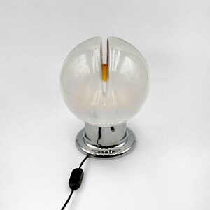 May include: A white glass table lamp with a chrome base and a split globe design. The lamp has a black cord and switch.
