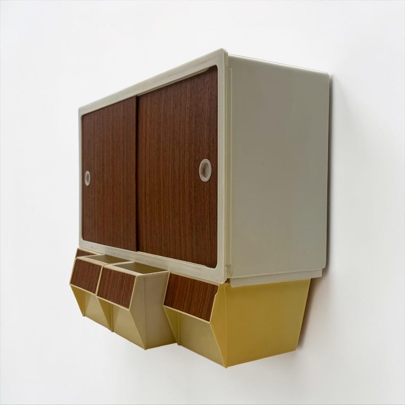 K&ouml;nnte beinhalten: Eine Wandmontage-Schrank mit Schiebet&uuml;ren und drei unteren F&auml;chern. Der Schrank hat einen cremefarbenen Rahmen, Holzt&uuml;ren und gelbe und cremefarbene Unterteile. Das Design ist im Retro-Stil.