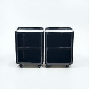 Peut inclure: Deux tables de chevet noires assorties avec une finition brillante. Chaque table a deux tiroirs et repose sur de petites roulettes. Les dessus des tables sont d'une couleur plus claire, créant un contraste avec le noir.