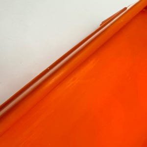 May include: A close-up of a vibrant orange, glossy surface. The image is dominated by the bright orange color, with a diagonal line creating a contrast against a white background. The surface appears smooth and reflective.