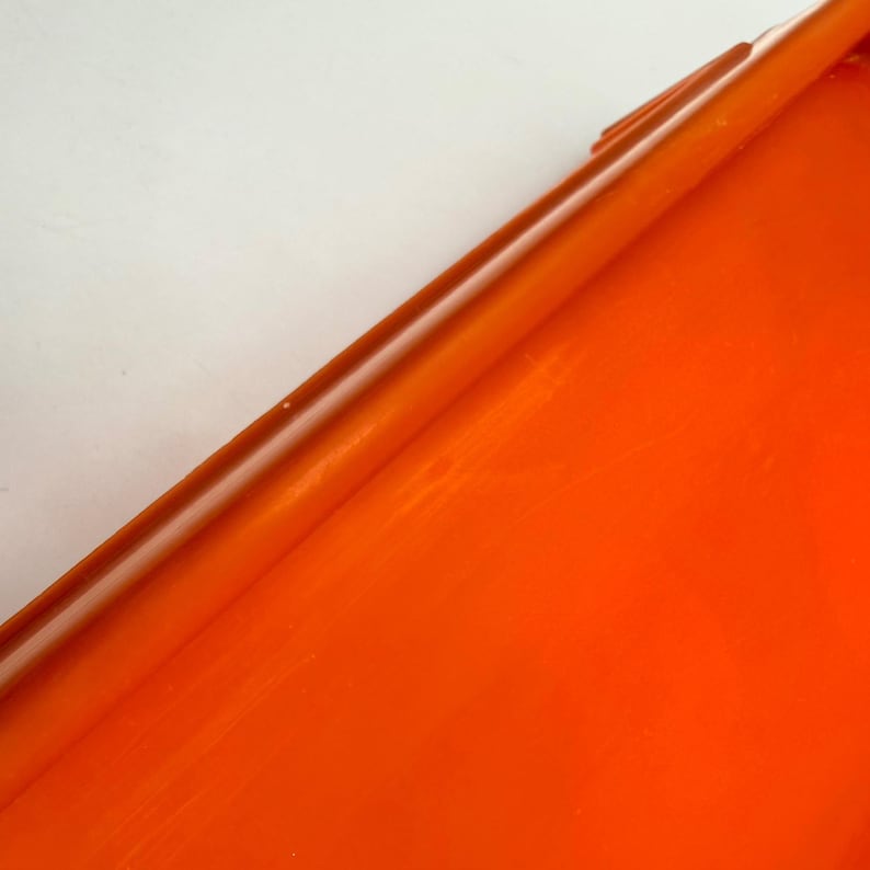 May include: A close-up of a vibrant orange, glossy surface. The image is dominated by the bright orange color, with a diagonal line creating a contrast against a white background. The surface appears smooth and reflective.