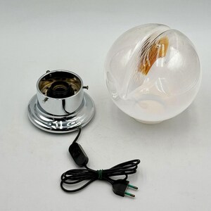 May include: A chrome and glass table lamp with a white globe and a brown and white patterned design. The lamp has a black cord and a switch.