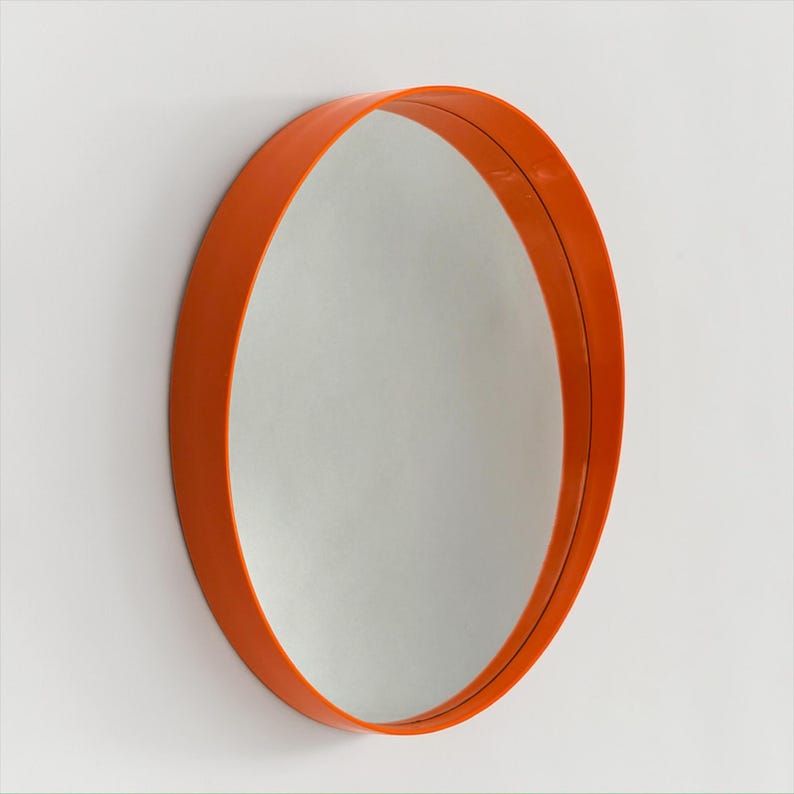 May include: An orange, round mirror with a simple, modern design. The mirror is mounted on a white wall, and the frame is a vibrant shade of orange. The circular shape and bold color make it a striking decorative piece.