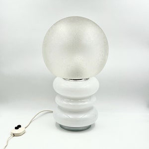 May include: White table lamp with a frosted glass globe shade and a white ceramic base with a stacked ring design.