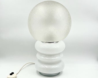May include: White table lamp with a frosted glass globe shade and a white ceramic base with a stacked ring design.