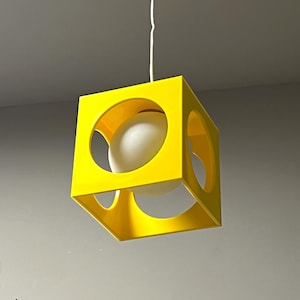 May include: A yellow cube-shaped pendant light fixture with a white globe inside. The globe is visible through a circular opening in the cube.