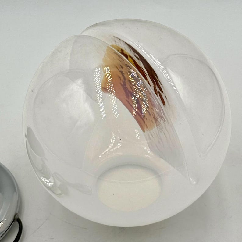 May include: A white glass globe with a brown and pink swirl design. The globe has a hole in the bottom.