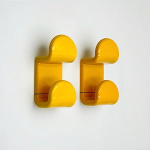 Peut inclure: Deux patères murales jaune vif au design incurvé. Chaque patère a une base rectangulaire avec un crochet supérieur et inférieur arrondis. Elles sont fixées sur une surface blanche.