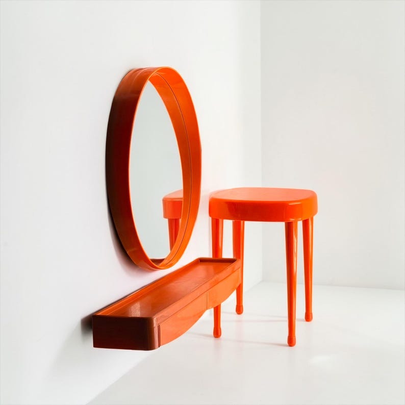 May include: An orange, modern-style vanity set. The set includes a round mirror, a rectangular shelf, and a small stool. The mirror and shelf are mounted on a white wall. The stool has four legs.