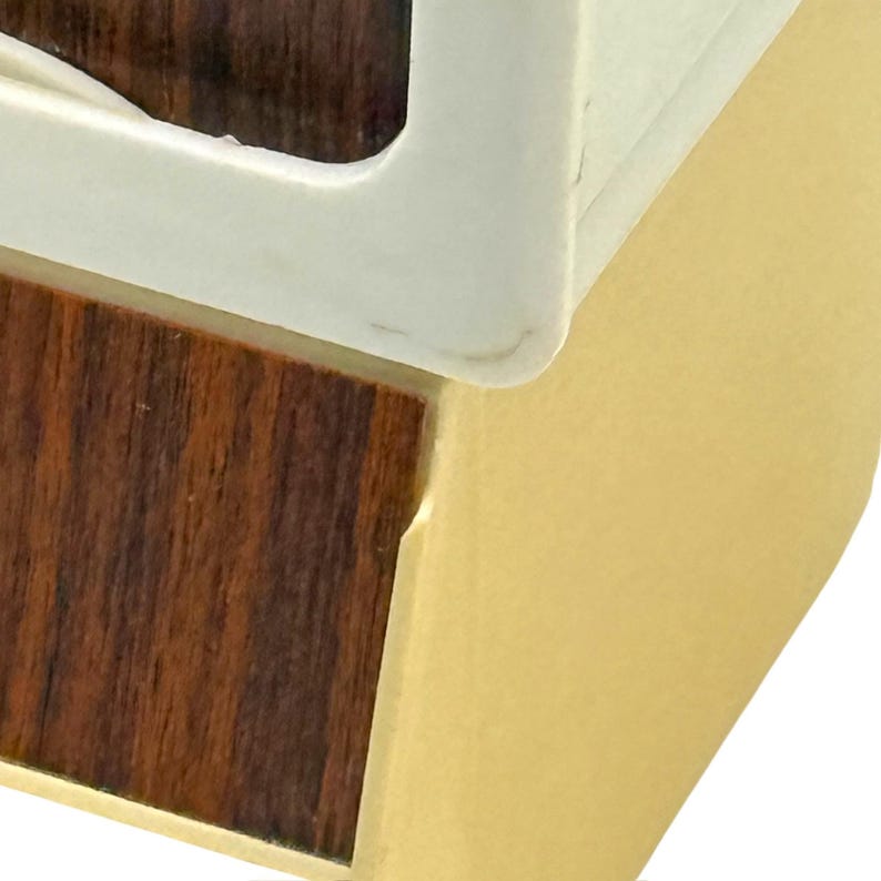 K&ouml;nnte beinhalten: Nahaufnahme einer Ecke einer Holzkiste mit wei&szlig;em Rahmen und goldfarbener Seite. Die Holzmaserung ist im dunkelbraunen Bereich sichtbar. Der wei&szlig;e Rahmen hat eine abgerundete Ecke.