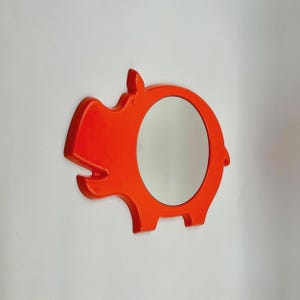 Puede incluir: Espejo de pared con forma de hipopótamo naranja con un espejo redondo en el centro.