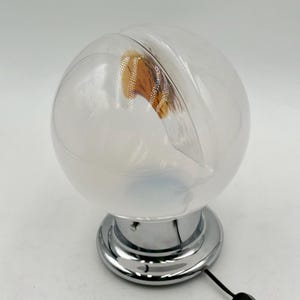 May include: A white glass globe table lamp with a chrome base and a brown and white patterned interior. The lamp has a cord and plug.