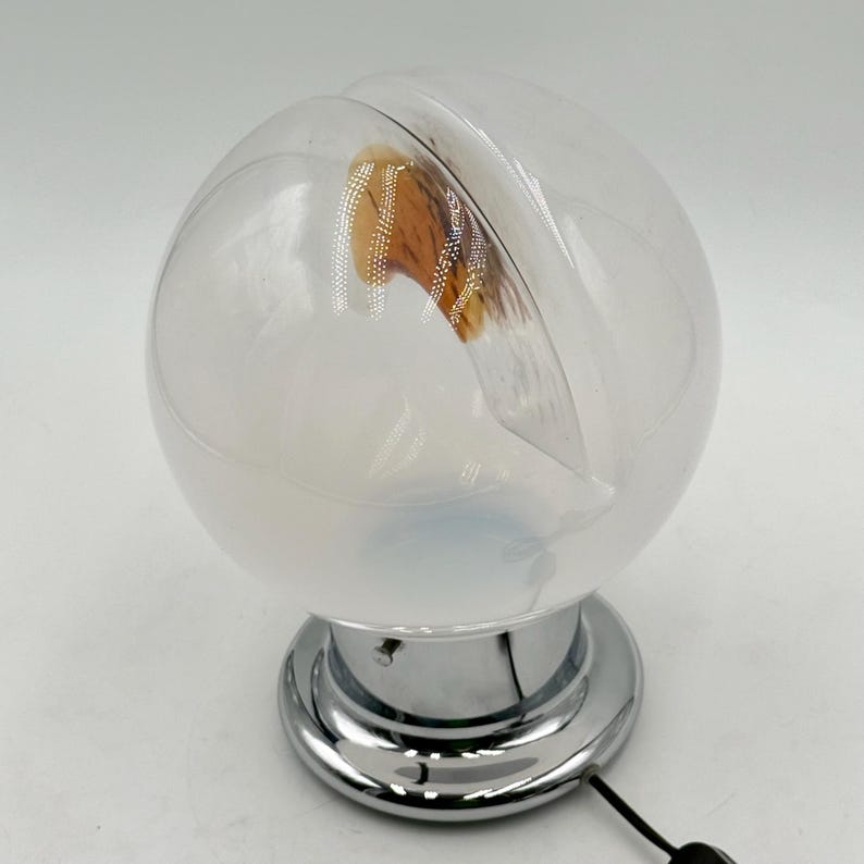 May include: A white glass globe table lamp with a chrome base and a brown and white patterned interior. The lamp has a cord and plug.