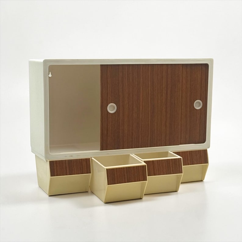 K&ouml;nnte beinhalten: Ein Vintage-Wandschrank mit Schiebet&uuml;r und drei kleinen Schubladen. Der Schrank ist cremefarben mit einer Schiebet&uuml;r und Schubladenfronten in Holzoptik. Das M&ouml;belst&uuml;ck hat ein Retro-Design.
