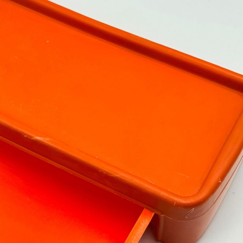 May include: Bright orange plastic storage container with a rectangular shape. The container has a lid and a drawer. The color is a vibrant, solid orange.
