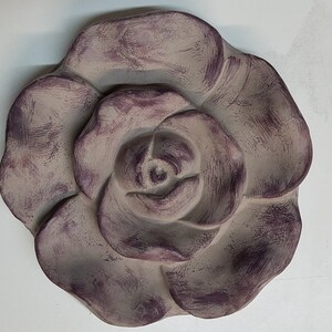 Pu&ograve; includere: Una grande rosa decorativa di colore grigio-viola realizzata in gesso o ceramica. La rosa ha una superficie testurizzata ed &egrave; una rappresentazione 3D di un fiore.