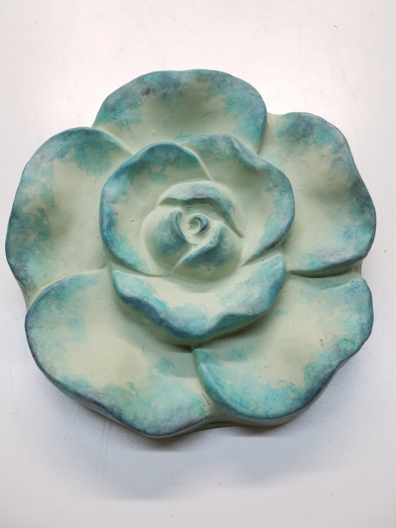 Pu&ograve; includere: Una scultura di rosa in ceramica di colore verde chiaro e blu. La rosa &egrave; scolpita in uno stile realistico con un centro e petali dettagliati.