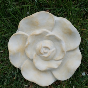 Pu&ograve; includere: Una scultura di rosa in ceramica bianca con un design dettagliato. La rosa &egrave; seduta su un letto di erba verde.