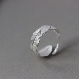 Op de afbeelding: Een zilveren ring met een veren ontwerp. De ring is open en verstelbaar.