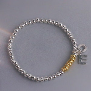 May include: A silver beaded bracelet with a gold charm and a silver letter 'E' charm.