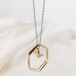May include: A silver chain necklace with a gold hexagonal pendant featuring a small gold bee charm.