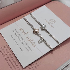 Puede incluir: Dos pulseras de cuentas plateadas con un dije de estrella. Un dije es plateado y el otro es de oro rosa. Las pulseras están empaquetadas en una caja blanca con el texto "soul sisters" y "lleva estas pulseras juntas como un recordatorio de que nuestro amor es para siempre. Una para ti, una para mí."